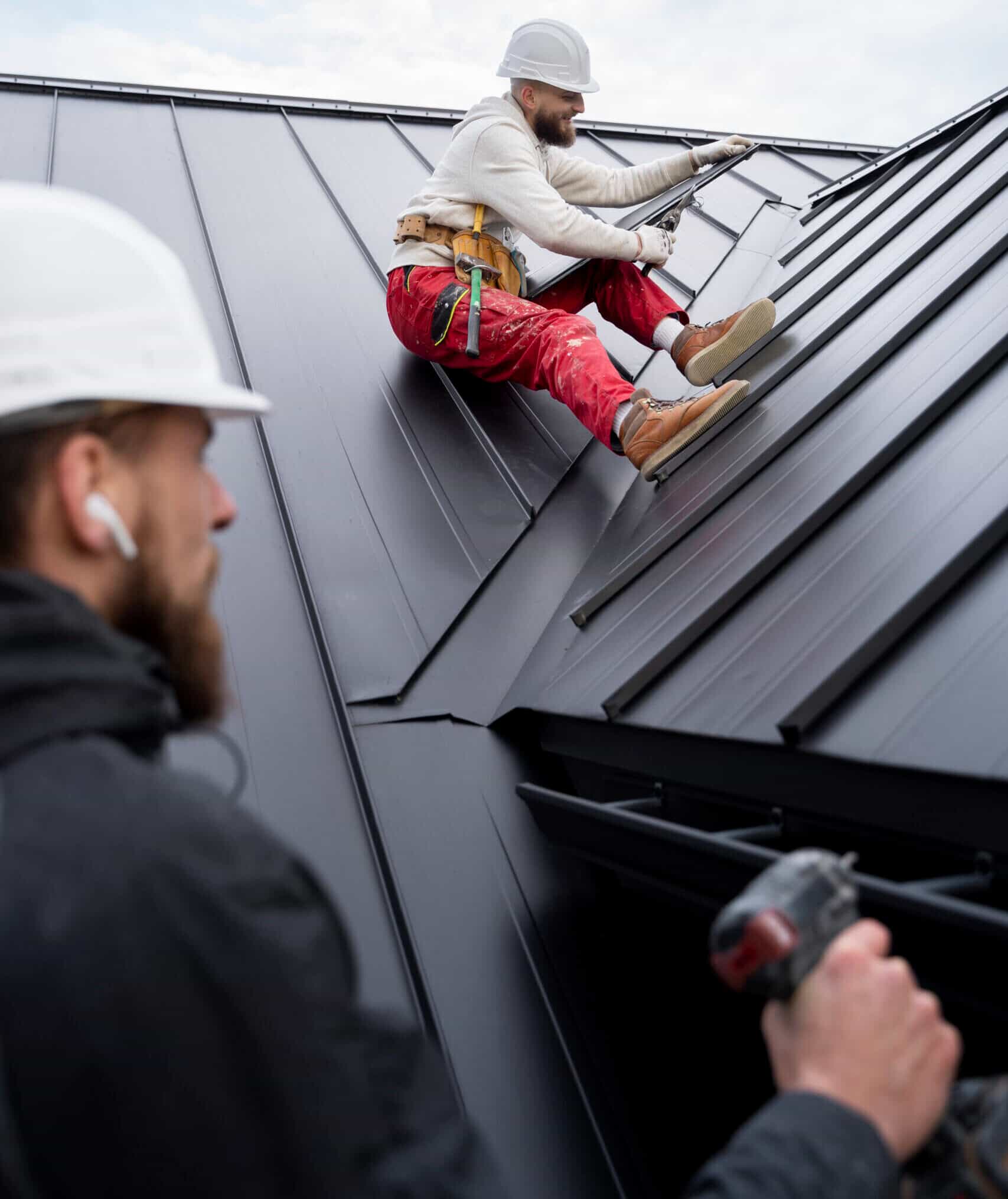 Two roofing contractors working on a residential roof installation with clay tiles staged across the surface
